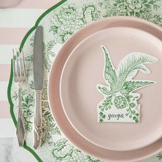 a pink plate with a green bird and name tag on it next to silverware