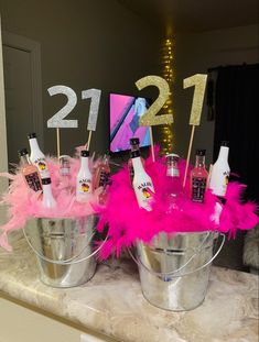 two buckets filled with drinks and pink feathers sitting on top of a marble counter