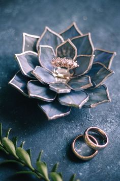 two wedding rings sitting on top of a flower shaped plate next to another ring holder