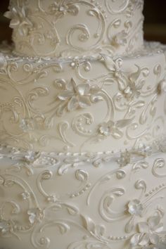 a three tiered white wedding cake with flowers on the top and sides, decorated with pearls