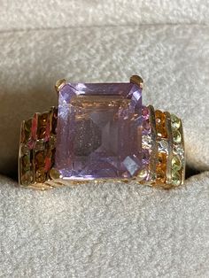 Can you say amazing??  This beauty is really big!  This ring is hallmarked 10K and guaranteed to be such.  The star of the show is the center 12mm x 10mm amethyst stone.  As if that weren't enough, flanking the center stones are 10 vertical stones:  8-2mm peridot, citrine and amethyst stones, all channel set. Cascading through the middle of the side stones are 6-1 point diamonds.  This gorgeous ring is a size 7 1/2 and weighs in at 5.8 grams. It big, bold and a real showstopper!! Yellow Gold Amethyst Ring, Gold Amethyst Ring, Amethyst And Diamond Ring, Amethyst Stones, Gorgeous Ring, Channel Set, Amethyst Stone, Amethyst Ring, Rings Statement