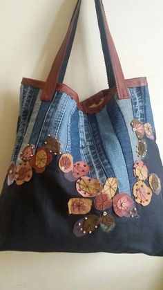 a denim bag with buttons and leather handles hanging on a wall next to a white wall