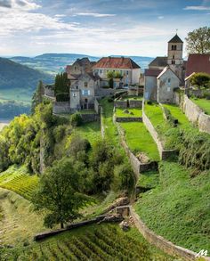 an old village on top of a hill with lots of green grass and trees in the foreground