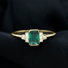 an emerald and diamond ring sitting on top of a black cloth