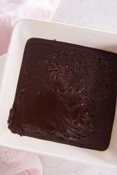 a square chocolate cake sitting on top of a white plate next to a pink napkin