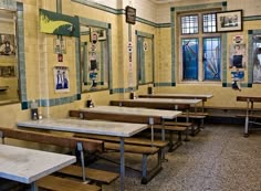 an empty classroom with tables and benches in front of large windows, decorated with pictures on the wall