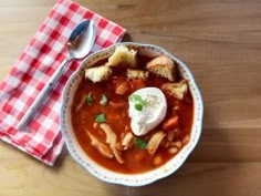 a bowl of soup with bread and sour cream on the side, sitting on a checkered napkin