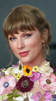 a woman with blonde hair wearing a flowery dress and necklace in front of her face