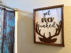 a wooden sign that says get buck naked hanging on the wall next to a shower curtain