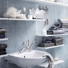 a white sink sitting under a bathroom mirror next to shelves filled with towels and other items