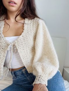 a woman sitting on top of a bed wearing a white sweater