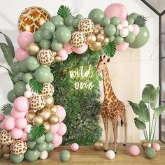 a giraffe standing in front of a jungle backdrop with balloons and greenery