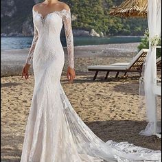 a woman standing on top of a sandy beach wearing a wedding dress with long sleeves