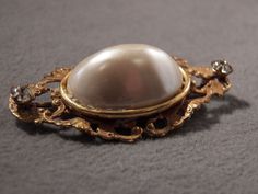 I am offering you this elegant vintage gold tone brooch. There are so many exciting design elements to this piece, it is sensational! It features a lovely fancy gold tone filigree design and a large convex oval shaped faux pearl stone and rhinestones, so fabulous! The brooch measures approx. 1 1/4 inches in length and 2 inches in width, and its breathtaking There is a secure safety locking closure pin back. Glamorous brooches like this are a hot current fashion trend this season, a must for your Elegant Gold Filigree Brooches, Victorian Gold Brooches With Jewels, Antique Gold Brooches With Jewels, Heirloom Gold Brooches For Evening, Heirloom Gold Evening Brooches, Victorian Gold Brooches For Evening, Gold Jeweled Brooches For Formal Occasions, Elegant Gold Jeweled Brooches, Formal Gold Jeweled Brooches