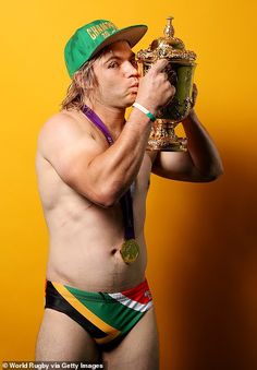 a shirtless man wearing a green hat and holding a trophy in his right hand