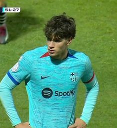 a man standing on top of a soccer field wearing a blue shirt and holding his hands on his hips