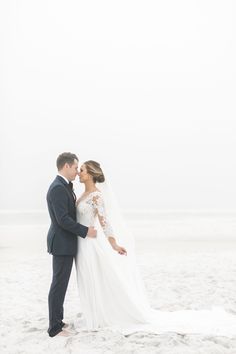 a bride and groom standing on the beach