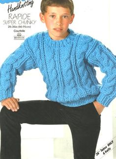 a young boy in a blue sweater and black pants sitting on a white chair with his hands on his hips