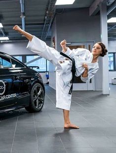 a woman is doing karate in front of a black car and another person standing next to her