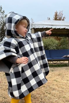 a little boy dressed in a black and white checkered ponchy with yellow rubber boots