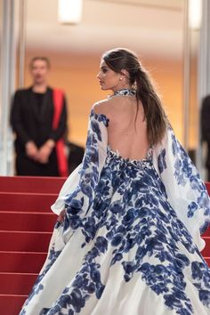 a woman in a blue and white dress is walking down the red carpeted stairs