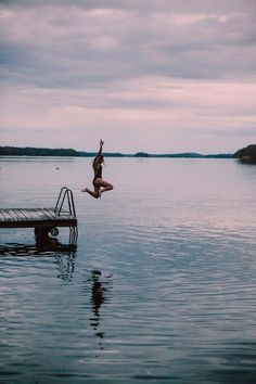 a person jumping into the water from a dock in front of a body of water