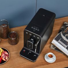 an espresso machine sitting on top of a wooden table next to a bowl of fruit