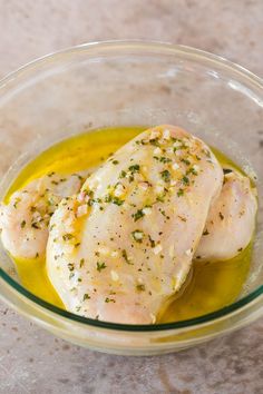 two pieces of chicken are in a bowl with olive oil and parsley on the side