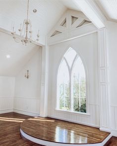 an empty room with a large arched window and wood flooring in front of a chandelier