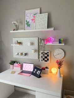 a white desk topped with a laptop computer sitting on top of a white desk next to a clock