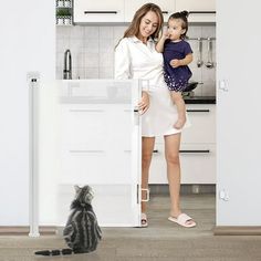 a woman holding a baby standing next to a cat