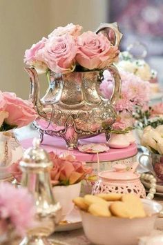 a table topped with lots of pink flowers and teapots filled with cookies on top of it