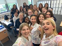 a group of young women standing next to each other in front of a classroom desk