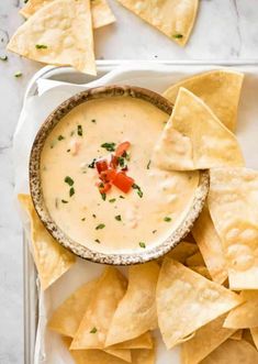 tortilla chips and dip in a white bowl on a plate with crackers