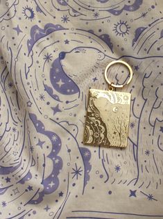 a gold keychain is sitting on top of a blue and white paisley print fabric