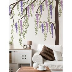 a white couch sitting under a tree with purple flowers on it's branches in front of a wall mural