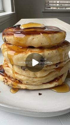 a stack of pancakes covered in syrup on top of a white plate next to a window