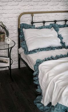 a bed with white sheets and blue ruffled bedspread next to a brick wall