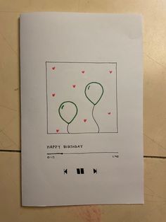 a birthday card with two balloons and hearts on the front, sitting on a tile floor