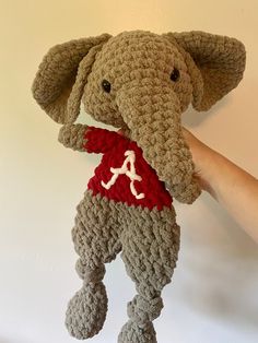 a crocheted elephant with a red shirt on it's chest is held up by a hand