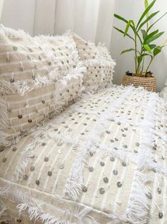 a bed with white sheets and pillows on it next to a plant in a basket