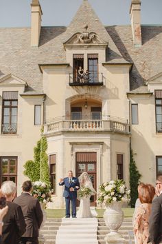 a bride and groom are standing in front of a large house with flowers on the steps