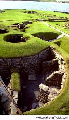 an aerial view of a grassy area with water in the background and several mounds on the ground