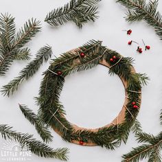 a wreath made out of branches and red berries is surrounded by pine needles on a white background