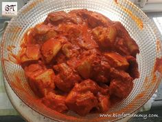 a glass bowl filled with red sauce and cubed meatballs on top of a table