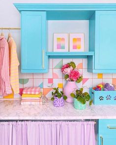 a kitchen with blue cabinets and pink flowers on the counter top next to a potted plant