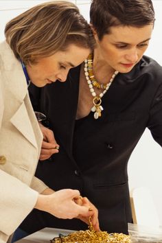 two women standing over a cake with gold sprinkles on it