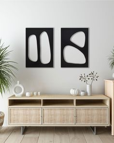 two black and white paintings on the wall next to a wooden shelf with vases