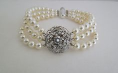 "This vintage inspired bracelet has a Victorian style rose with Swarovski crystals and three strands of Swarovski pearls in ivory/cream. Pendant measures just under 1\" in diameter, pearls measure 6 mm. Bracelet measures approximately 7 1/4\" long. Swarovski pearls are available in different colors, and can be made in different finishes and lengths. Please choose yours at checkout. This is the perfect addition for your vintage inspired wedding or special occasion event. What a romantic piece for Vintage Pearl Bracelet For Wedding, Elegant Cream Pearl Bracelet For Wedding, Elegant Beaded Cream Bracelets, Elegant Cream Beaded Pearl Bracelet, Elegant Cream Pearl Bracelet, Elegant Cream Pearl Beaded Bracelets, Elegant Cream Pearl Bracelets, Elegant Cream Beaded Bracelets For Parties, Elegant Pearl Bracelet For Mother Of The Bride