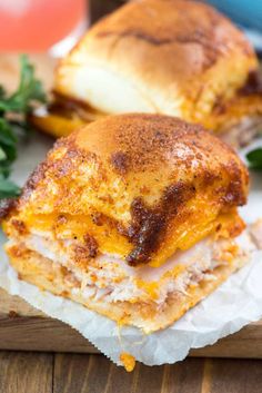 two sandwiches with cheese and meat sitting on wax paper next to some parsley sprigs